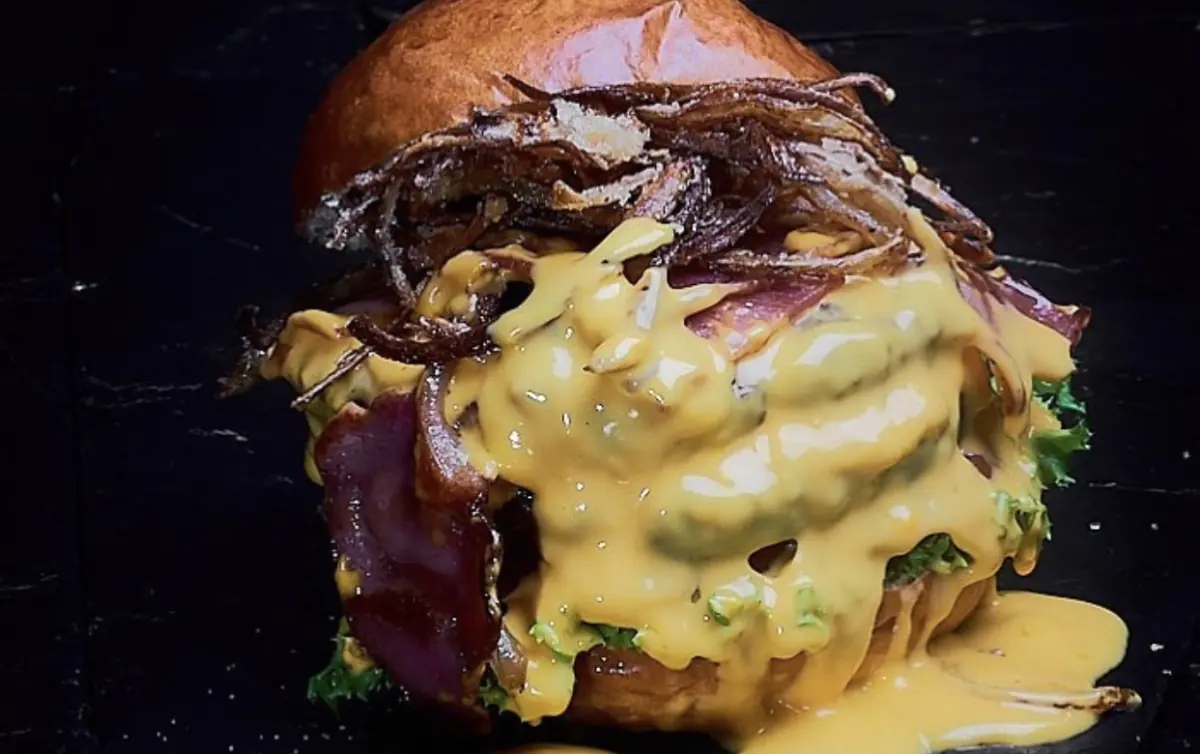 Hamburguesa bañada en salsa de queso con cebolla crocante y papas rústicas